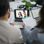 Two professionals conduct a virtual job interview using laptops in a modern office.